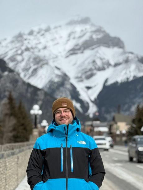 Alec in a blue ski jacket and a brown toque, a snowy mountain behind him